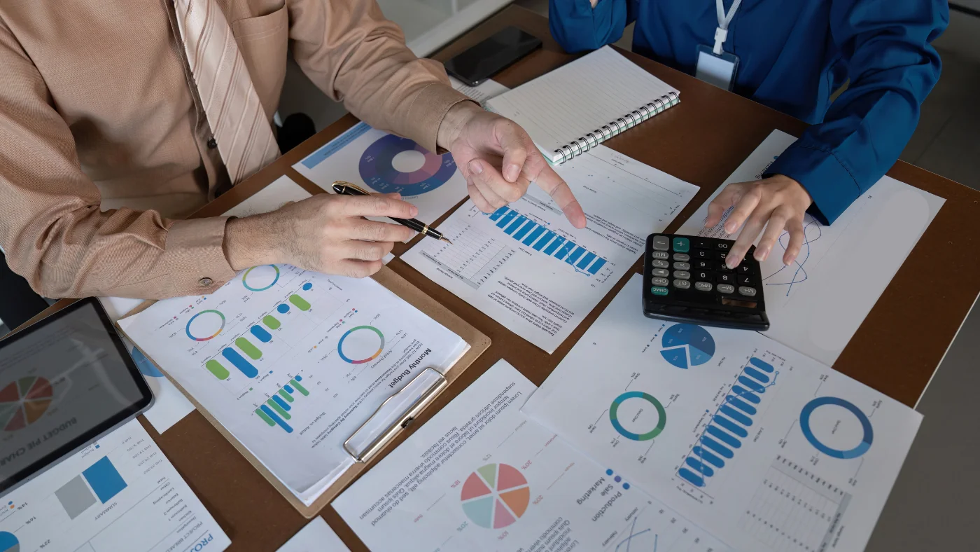 a table of printed out, colorful spreadsheets and two sets of hands