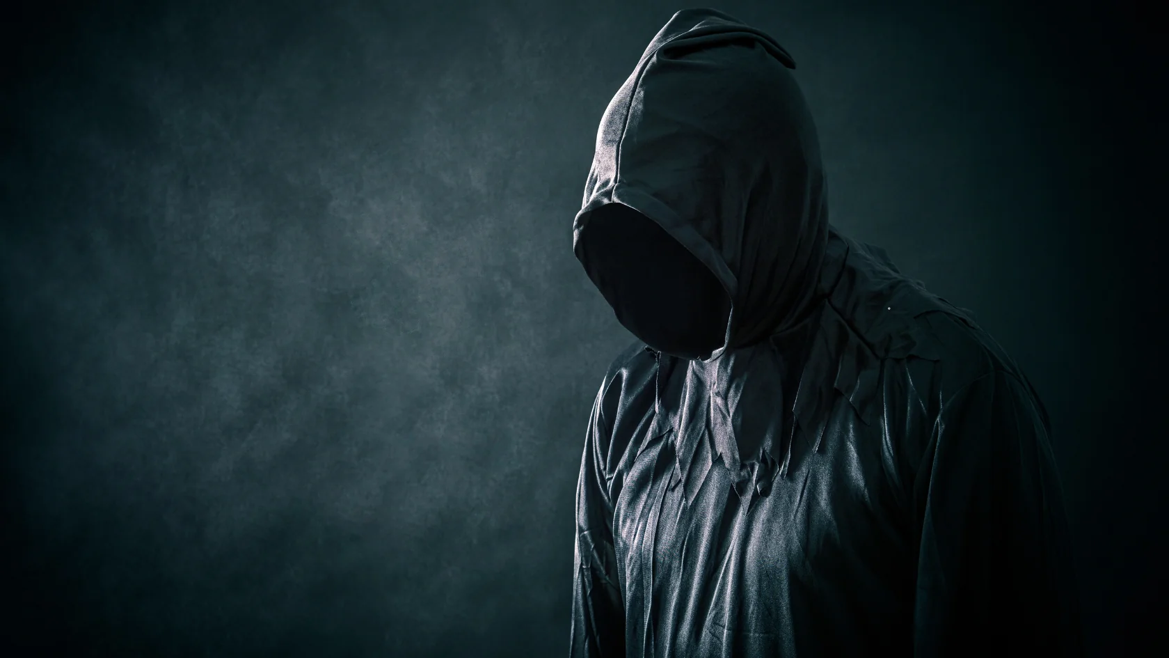 a shadowy figure wearing a black hooded sweater with their face hidde